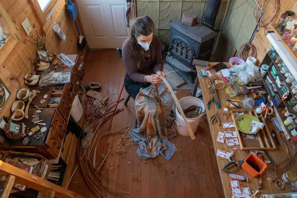 Quinn sits in her workshop and prepares materials to be used in basket weaving in The Plains, Ohio, on Feb. 8, 2022. Located in her backyard, the workshop is heated by a woodburning stove and also uses energy from the solar panels located on the structure’s side.  